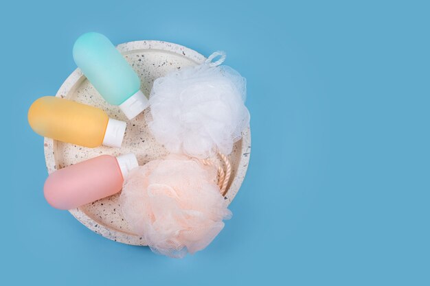 Contenants en plastique colorés pour shampoing, baume capillaire et gel douche avec des débarbouillettes sur un plateau en marbre. Produits cosmétiques pour spa et accessoires de bain sur fond bleu