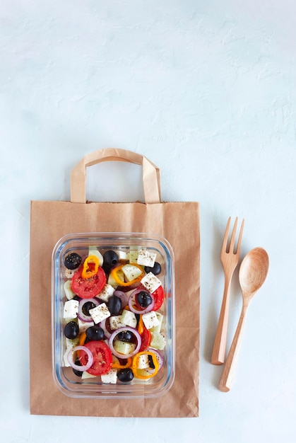 Conteneur avec salade grecque, couverts en bois, sur fond blanc, vue de dessus, espace de copie, concept d'alimentation saine et zéro déchet