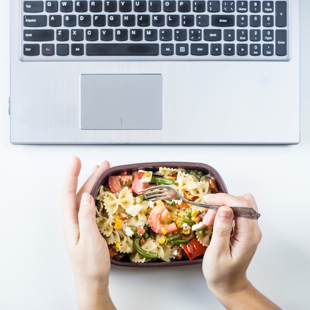 Photo conteneur avec salade avec des pâtes sur le lieu de travail près de l'ordinateur