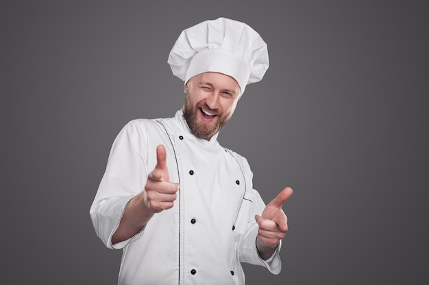 Contenu cuisinier masculin en uniforme de chef blanc pointant vers la caméra montrant que nous voulons que vous fassiez un geste pour le concept de recrutement