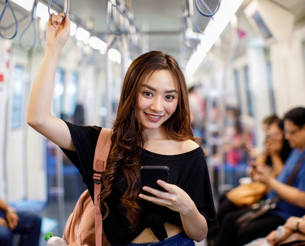 Contenu du train d'une femme asiatique et discutant sur les réseaux sociaux via un smartphone tout en tenant la main courante et en regardant la caméra. Communication et transport dans le concept de ville.