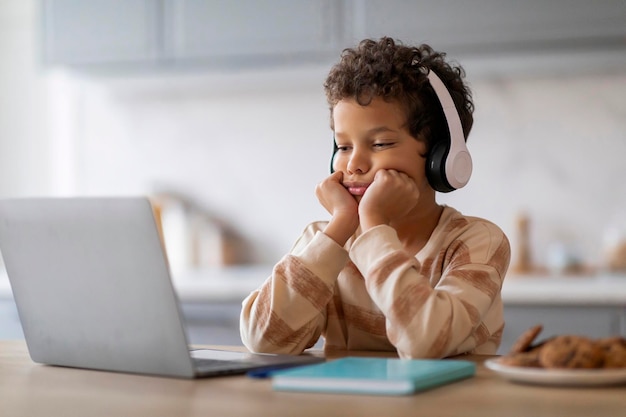 Contenu ennuyeux bouleversant petit garçon noir dans des écouteurs regardant l'écran de l'ordinateur portable