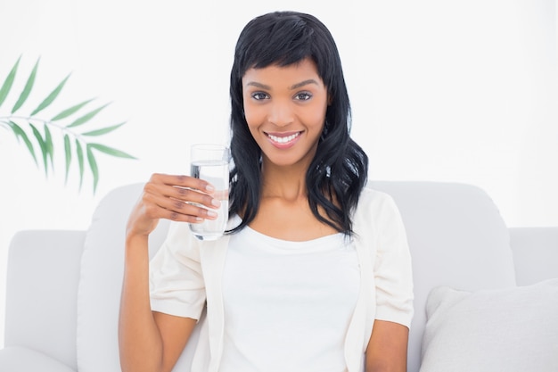 Contenu femme aux cheveux noire en vêtements blancs tenant un verre d&#39;eau