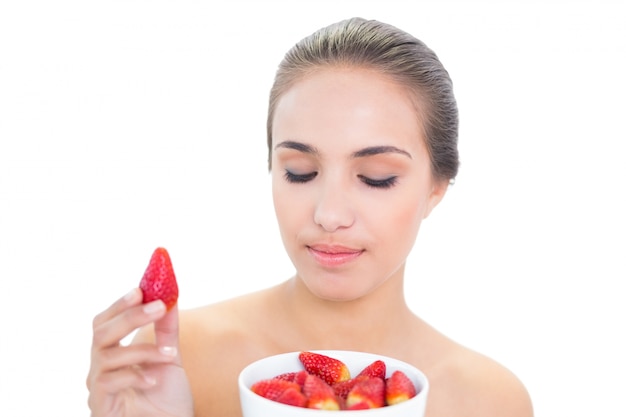 Contenu femme brune brandissant une fraise avec les yeux fermés