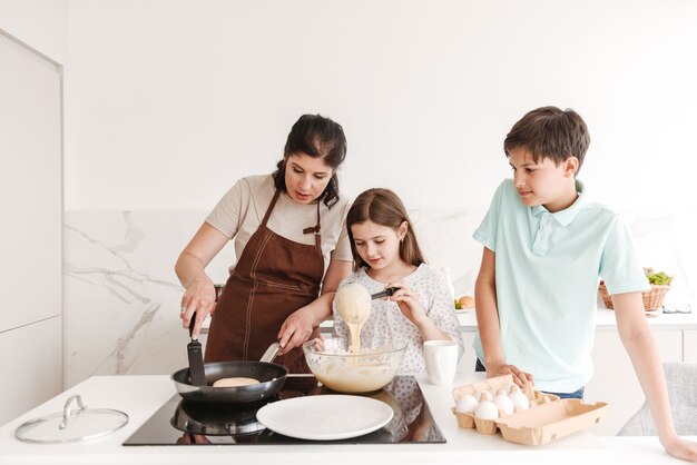 Contenu femme et enfants heureux cuisiner ensemble et faire frire des crêpes sur une cuisinière moderne dans la cuisine à la maison