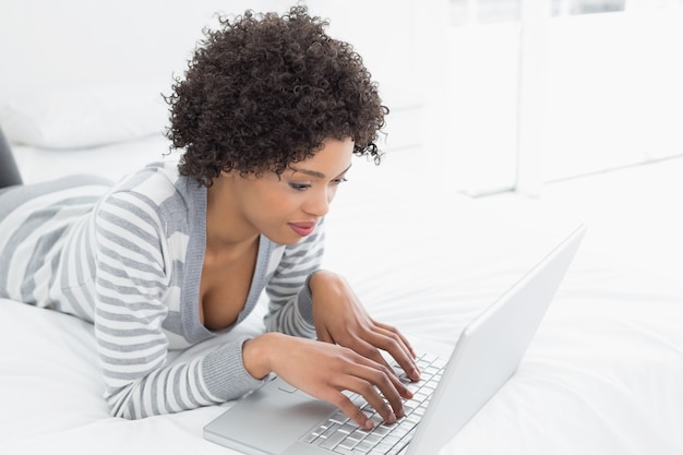 Contenu jeune femme à l&#39;aide d&#39;ordinateur portable au lit