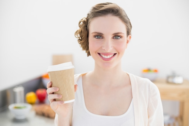 Contenu jeune femme tenant une tasse jetable debout dans sa cuisine