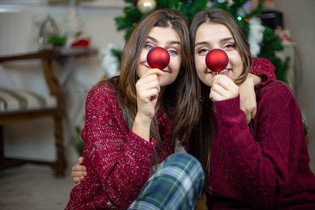 Contenu de jeunes femmes s'embrassant assis sur le sol et faisant le nez avec des boules d'arbre rouge