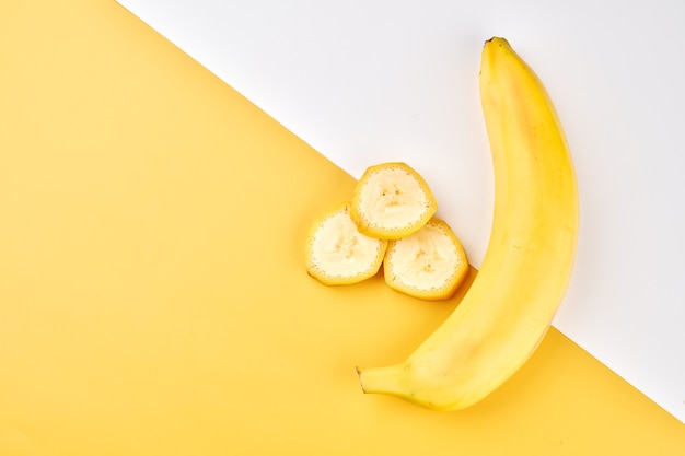 Contexte créatif de la banane. Fond jaune et blanc avec des bananes entières, pelées et tranchées