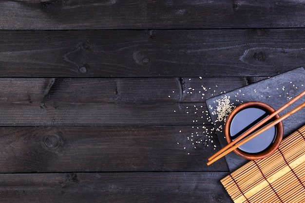 Contexte pour les sushis. Tapis de bambou et sauce soja sur table en bois noir. Vue de dessus avec espace copie