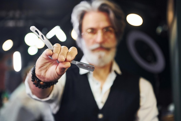 Photo contient l'équipement du salon de coiffure un homme âgé moderne et élégant aux cheveux gris et à la barbe est à l'intérieur