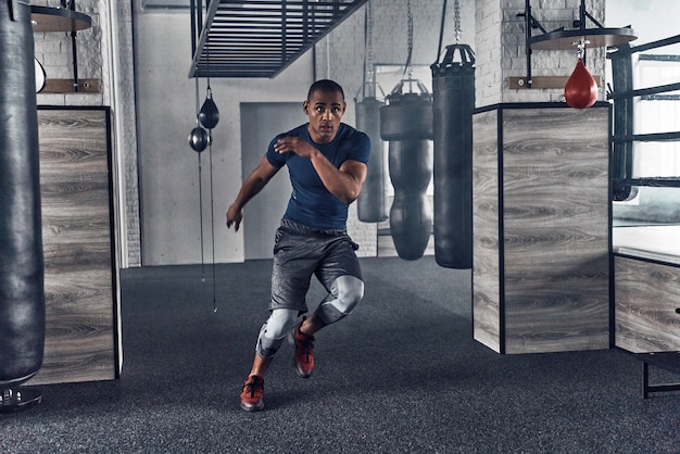 Continuez simplement à bouger. Toute la longueur du beau jeune homme africain en vêtements de sport en cours d'exécution