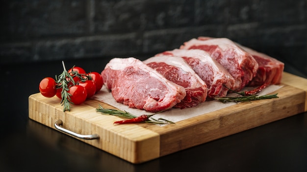 Contre-filet de steak de viande crue crue new york sur une planche de bois avec tomates et romarin