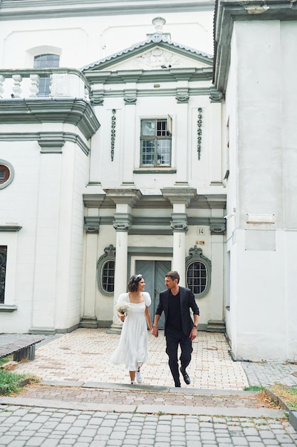 Contre le grand bâtiment de l'église Belle mariée avec son fiancé célèbre le mariage à l'extérieur