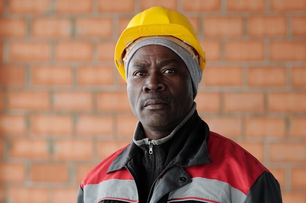 Contremaître afro-américain mature sérieux en vêtements de travail et casque de protection