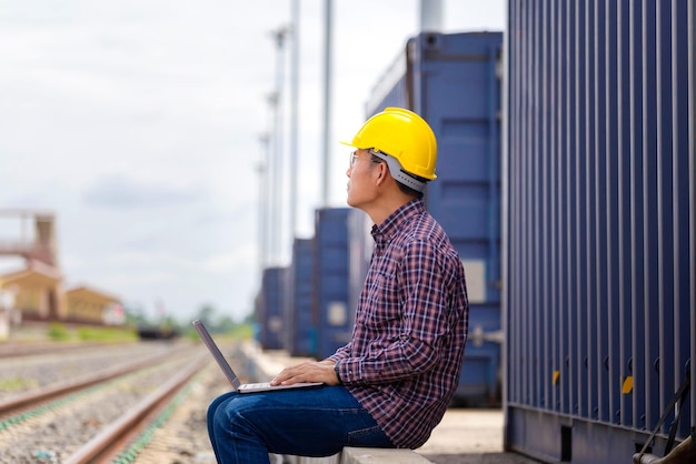 Contremaître en casque vérifiant les projets de transport ferroviaire à partir de la cargaison Ingénieur avec ordinateur portable Ouvrier industriel dans l'industrie des conteneurs de fret