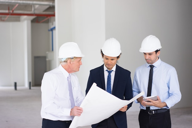 Contremaître confiant expliquant les tâches aux jeunes ingénieurs tout en montrant le plan de construction.