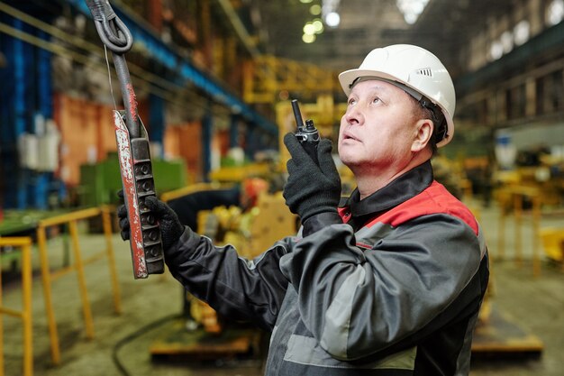 Contremaître mature en casque parlant en radio sans fil et appuyant sur les boutons de la télécommande tout en travaillant dans l'usine