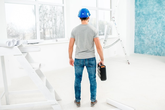 Contremaître ou ouvrier en uniforme avec des instruments debout dans l'intérieur blanc pendant la rénovation