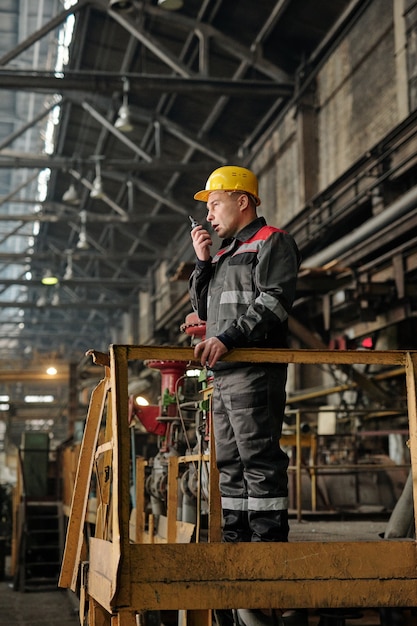 Contremaître en vêtements de travail parlant à la radio et contrôlant le travail dans l'usine