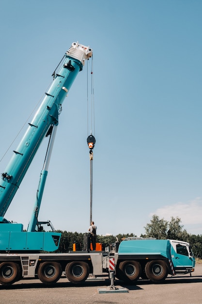 Photo le contrepoids est installé par un ouvrier méconnaissable sur une grande grue de voiture bleue et est prêt à travailler sur un site à côté d'un grand bâtiment moderne.