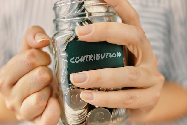 Photo contributions dans un bocal en verre une femme tient une bouteille de pièces d'éducation financière