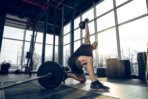 Contrôler. Jeune athlète caucasien musclé s'entraînant dans une salle de sport, faisant des exercices de force, pratiquant, travaillant sur le haut de son corps avec des poids et une balle. Fitness, bien-être, sport, concept de mode de vie sain.