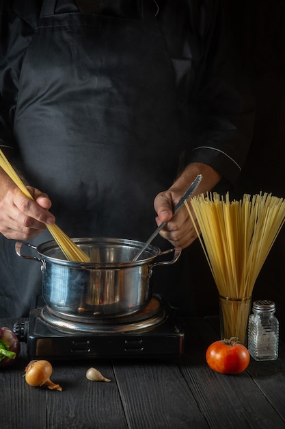 Cook prépare des pâtes italiennes dans une casserole avec des légumes. Gros plan des mains de cuisinier pendant la cuisson dans la cuisine du restaurant.