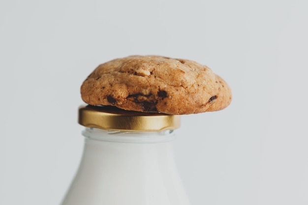 Un cookie avec des morceaux de chocolat se trouve sur une bouteille de lait sur fond blanc