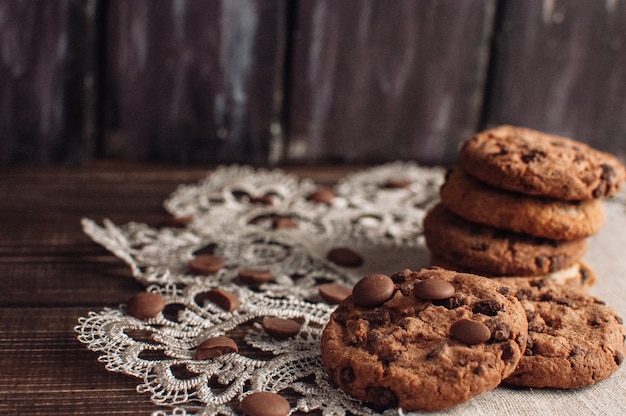 Cookies aux pépites de chocolat faits maison et de mie de chocolat concassé sur une table rustique sombre.