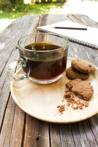 Cookies aux pépites de chocolat sur une plaque blanche avec un verre de café sur une table en bois.