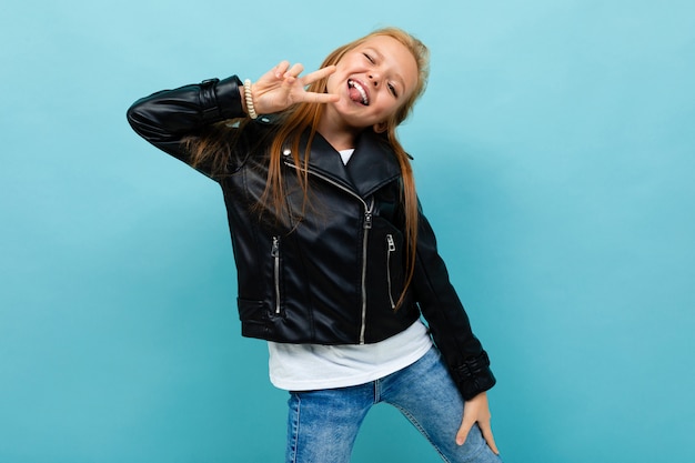 Cool adolescent fille en veste noire et jeans sourit isolatedd sur fond bleu