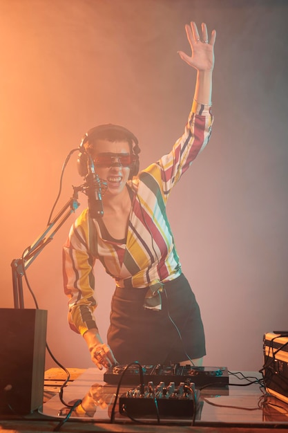 Cool disc-jockey utilisant un mélangeur pour jouer de la techno à la fête, mélangeant de la musique sur des platines dj avec des touches électriques en studio. Jeune artiste avec casque et microphone jouant au remix avec boutons de commande.