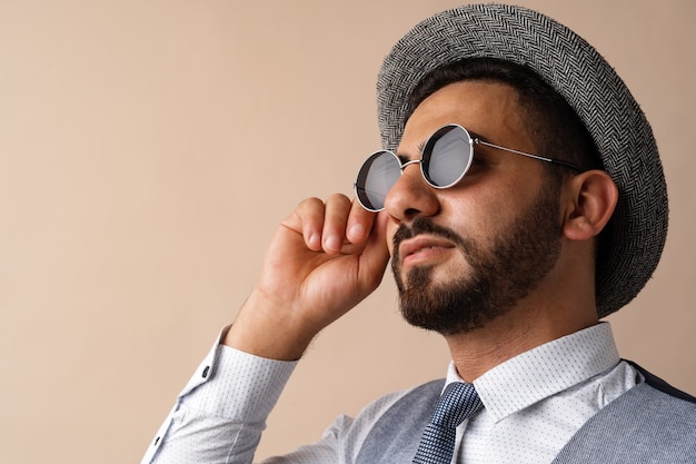 Cool homme égyptien en chapeau et lunettes de soleil posant sur fond beige