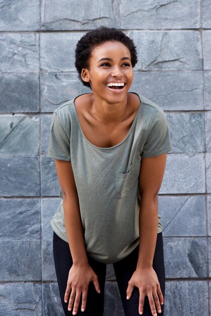 Cool jeune femme noire souriant avec t-shirt contre le mur gris