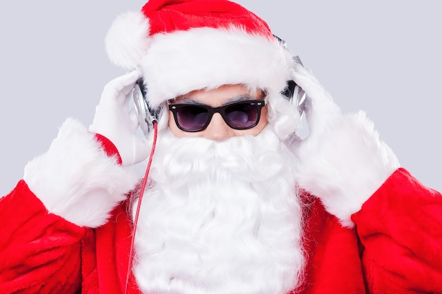 Cool Père Noël. Le Père Noël à lunettes de soleil ajustant ses écouteurs en se tenant debout sur fond gris