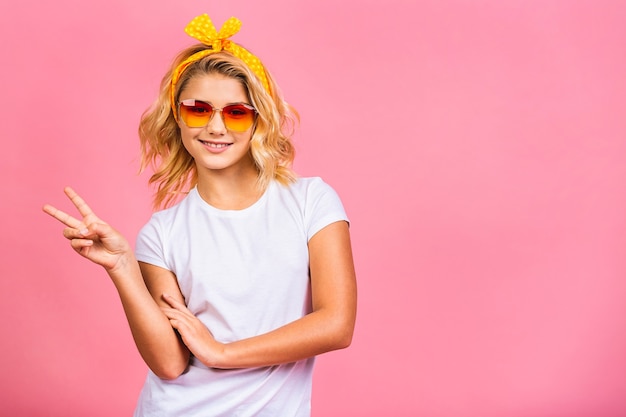 Cool petite fille blonde. Charmante adolescente en lunettes de soleil fantaisie souriant et posant pour la caméra