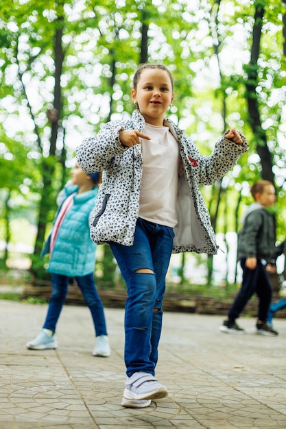 Cool petite fille marchant avec d'autres enfants dans une aire de jeux dans un parc verdoyant Vacances d'été dans le centre touristique du camp Marcher et jouer à l'extérieur activité sportive et loisirs de mode de vie sain