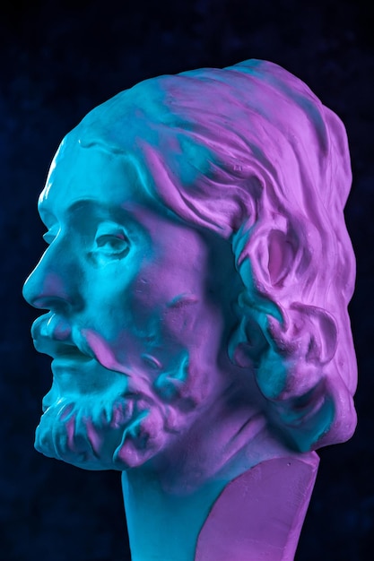 Copie en gypse colorée de l'ancienne statue de la tête de Jean-Baptiste pour les artistes sur un fond texturé sombre Sculpture en plâtre visage d'homme Jean baptisé Jésus Affiche d'art aux couleurs vives violettes et bleues