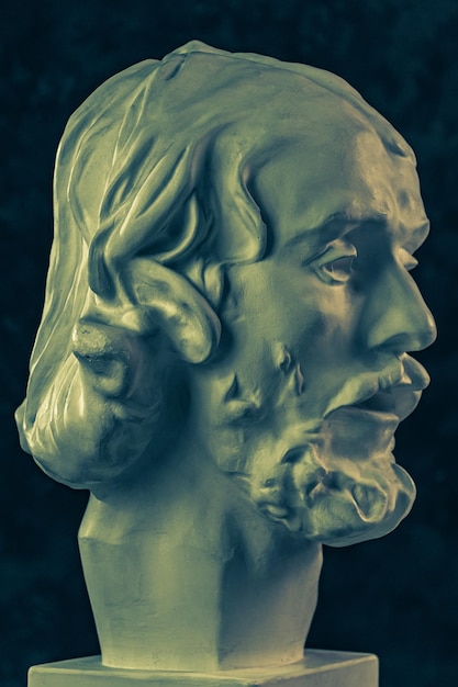 Copie en gypse colorée de l'ancienne statue de la tête de Jean-Baptiste pour les artistes sur un fond texturé sombre Sculpture en plâtre visage d'homme Jean baptisé Jésus Affiche d'art dans des couleurs vives jaunes et bleues