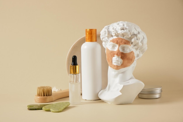 Une copie de la sculpture antique de David avec un masque d'argile cosmétique sur son visage des pinceaux de massage et des bouteilles cosmétiques