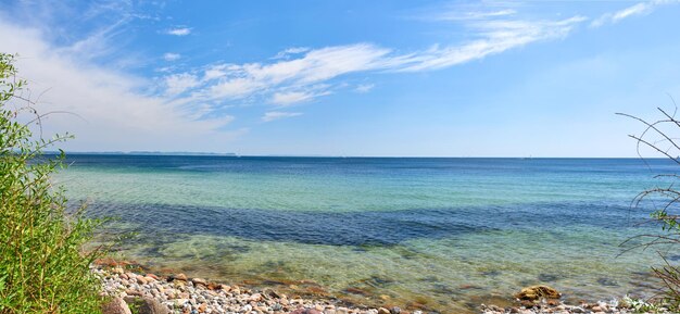 Copiez l'espace en mer avec un fond de ciel bleu nuageux à l'horizon Les vagues de l'océan se lavent sur des pierres sur une plage déserte Paysage pittoresque paisible pour des vacances d'été relaxantes et zen