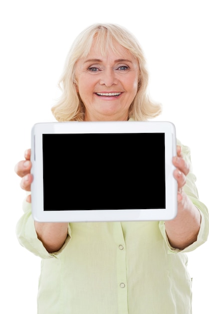 Copiez l'espace sur sa tablette numérique. Happy senior woman montrant sa tablette numérique et souriant tout en se tenant isolé sur fond blanc