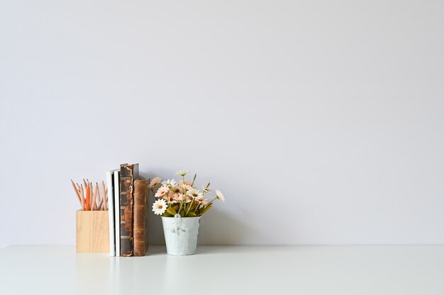 Copiez des livres de fournitures de bureau, des crayons et des fleurs sur un bureau blanc.