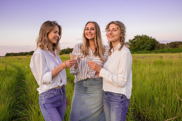 Copines buvant du champagne en pique-nique. Les femmes rient et s'amusent