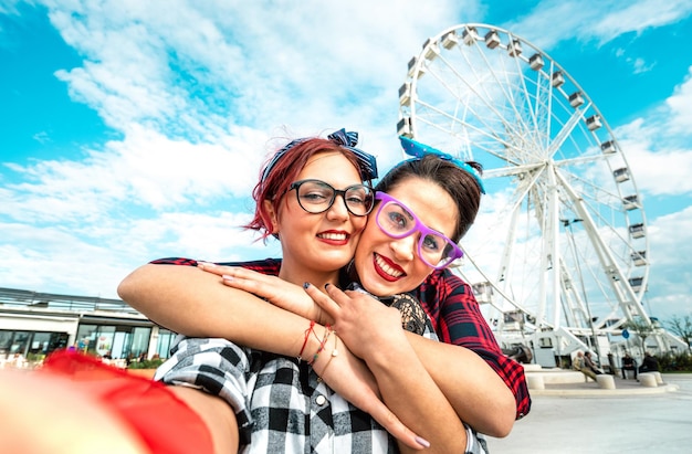 Copines de femmes heureuses prenant selfie à la grande roue sur l'espace public