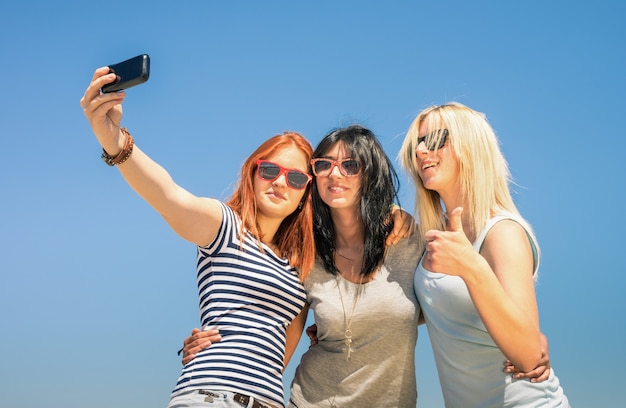 Copines heureuse prenant selfie contre le ciel bleu