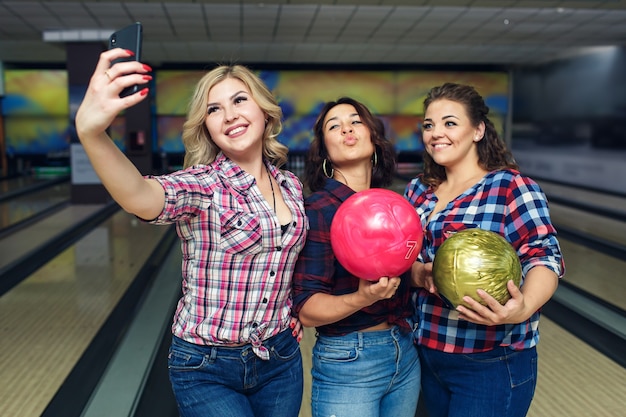 Des copines heureuses prennent selfie avec smartphone au club de bowling.