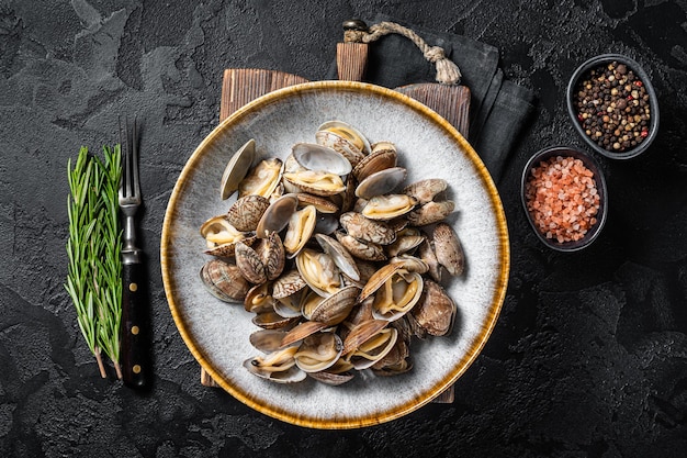 Coquilles cuites à la vapeur Palourdes vongole dans une assiette avec des herbes. Fond noir. Vue de dessus.