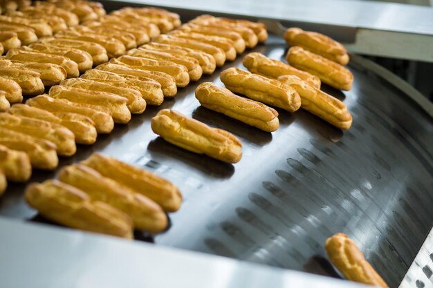 Coquilles d'éclairs jaunes sur le convoyeur Les éclairs glissent sur la ligne de convoyage Haut niveau de qualité Faire les meilleures confiseries